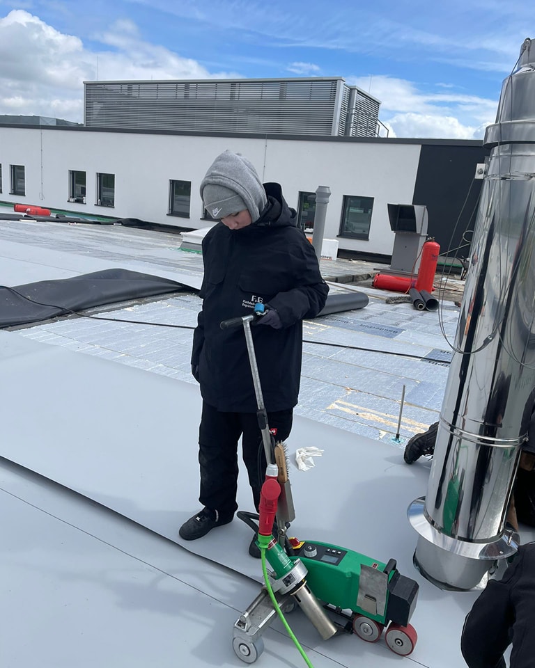 Dachdecker-Team verlegt eine weiße FPO-Dachmembran auf einem Flachdach – FuB Wiesbaden