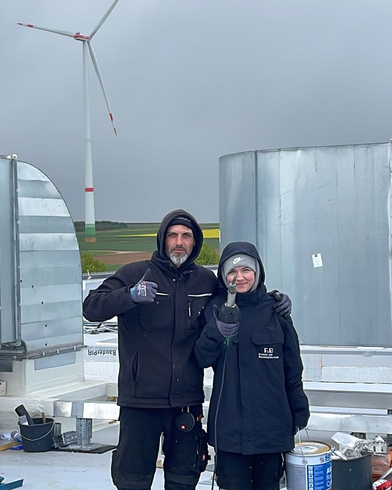 Zwei FuB-Dachdecker auf einem Industrieflachdach mit Windkraftanlage im Hintergrund