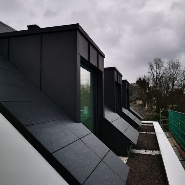 Modern gestaltete Dachlandschaft mit großflächigen Gauben und dunkler Metallverkleidung